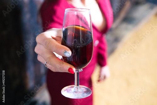 Young and beautiful businesswoman posing in her wine cellar in front of wooden wine barrels. The woman holds in her hands a glass of wine from her harvest and shows it to the camera. wine concept