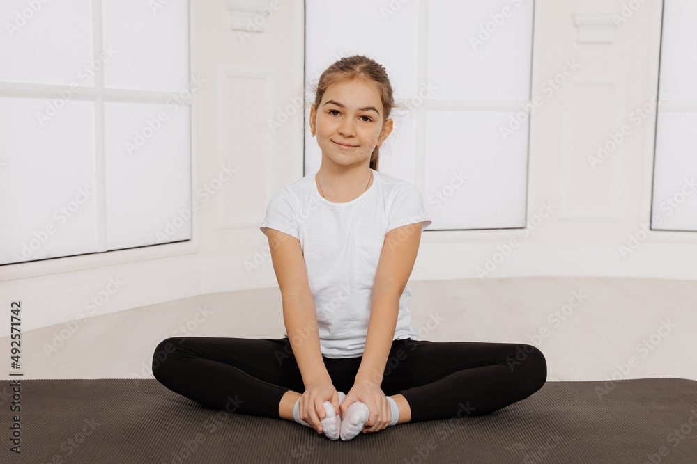 Young Cheerful kid girl doing exercises on fitness mat look at camera and smile Young Cheerful kid girl doing exercises on fitness mat look at camera and smile