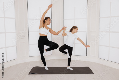  happy mother and child girl doing yoga while standing on the floor in the gym