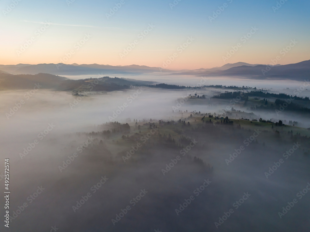Flight over fog in Ukrainian Carpathians in summer. Mountains on the horizon. Aerial drone view.
