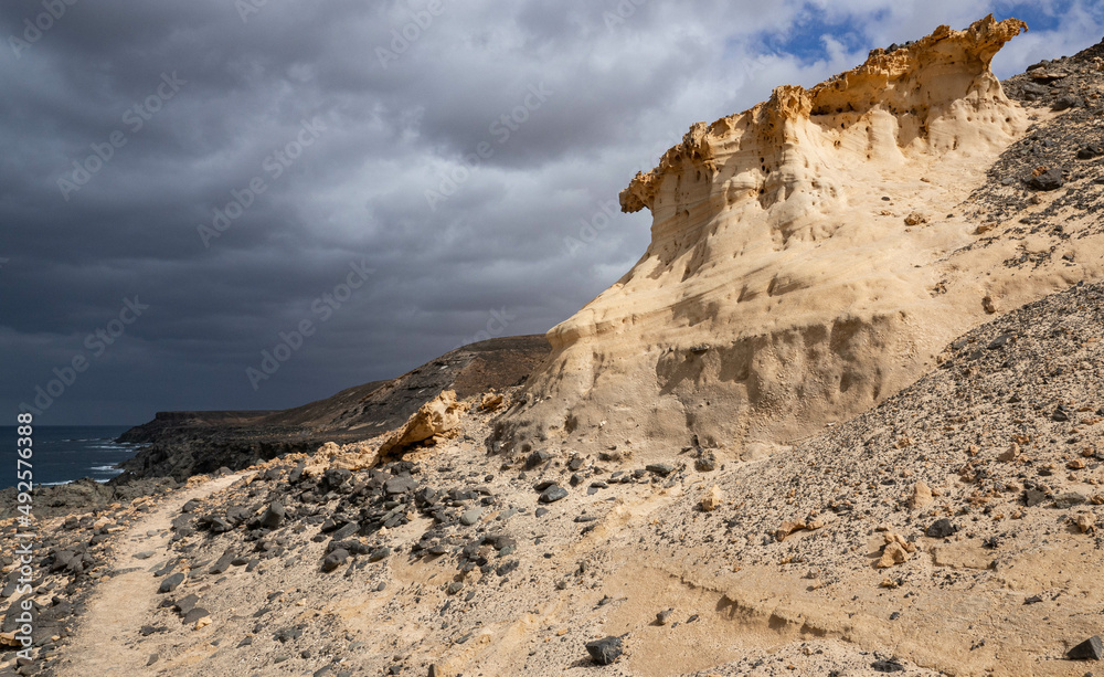 A coastal landscape on Fuerteventura. Spain, Canary Islands. Dark clouds, white rocks in the foreground are illuminated by the sun