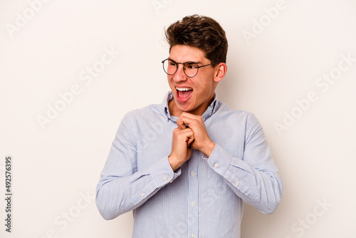 Young caucasian man isolated on white background keeps hands under chin, is looking happily aside.