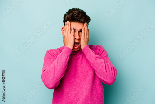 Young caucasian man isolated on blue background having fun covering half of face with palm.