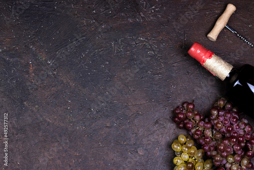 Ripe sweet grapes, wine bottle, on dark background. Flat lay, top view image with copy space.