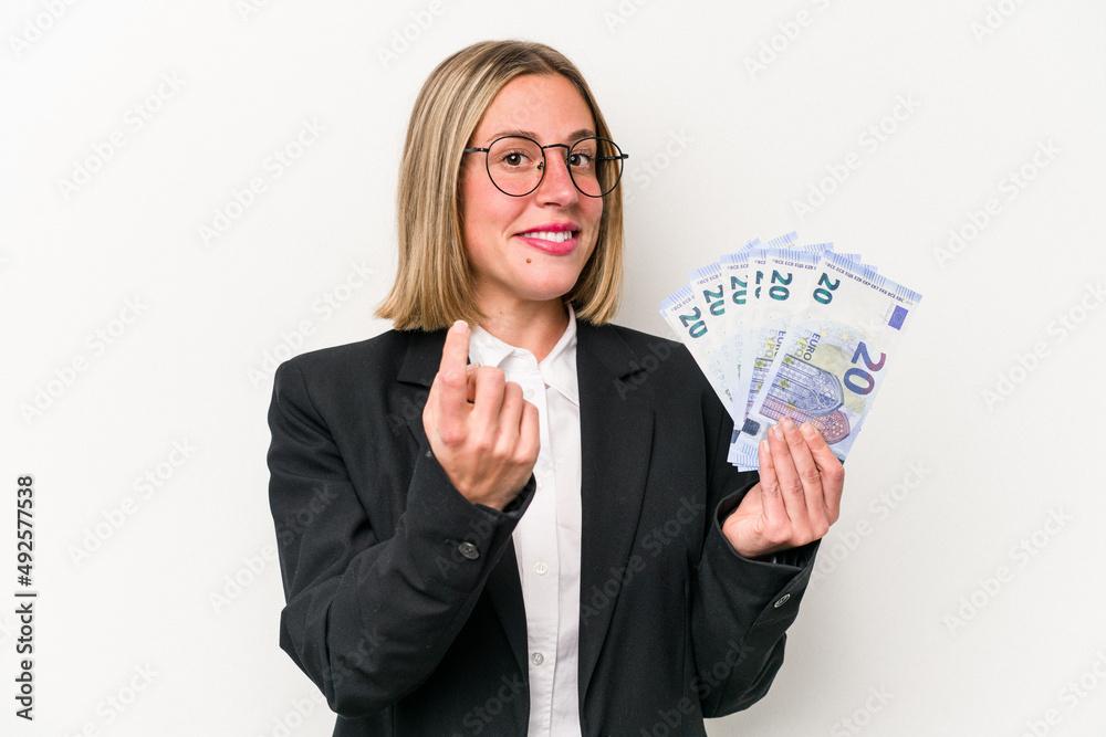 Young business caucasian woman holding banknotes isolated on white background pointing with finger at you as if inviting come closer. Young business caucasian woman holding banknotes isolated on white background pointing with finger at you as if inviting come closer.