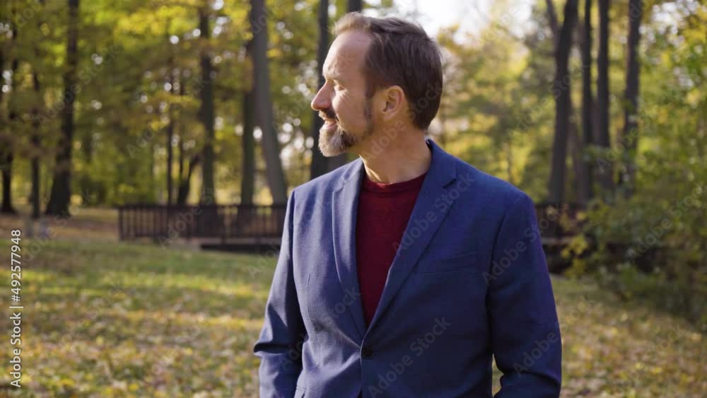 A middle-aged handsome Caucasian man walks and looks around with a smile in a park in fall - front view A middle-aged handsome Caucasian man walks and looks around with a smile in a park in fall - front view