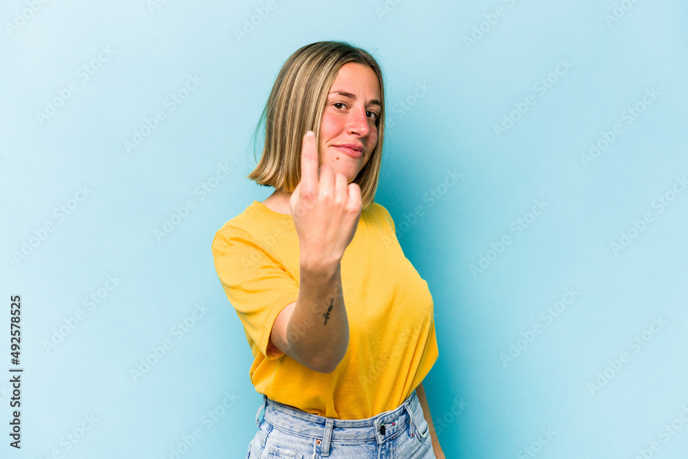 Young caucasian woman isolated on blue background pointing with finger at you as if inviting come closer.