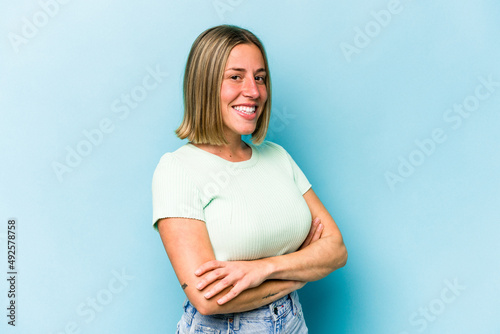 Young caucasian woman isolated on blue background who feels confident, crossing arms with determination.