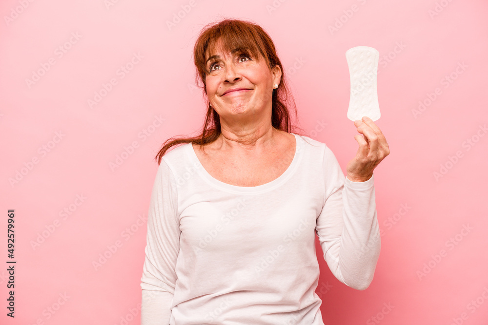 Middle age caucasian woman holding sanitary napkin isolated on pink background dreaming of achieving goals and purposes Middle age caucasian woman holding sanitary napkin isolated on pink background dreaming of achieving goals and purposes