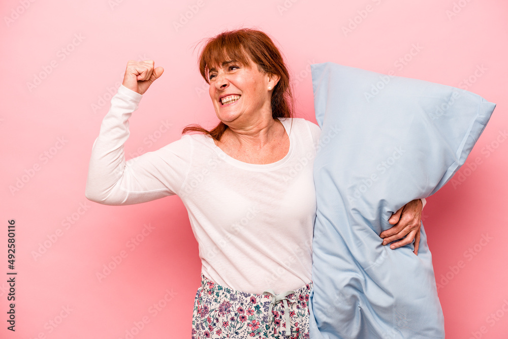 Obraz premium Middle age woman wearing a pajama isolated on pink background raising fist after a victory, winner concept.