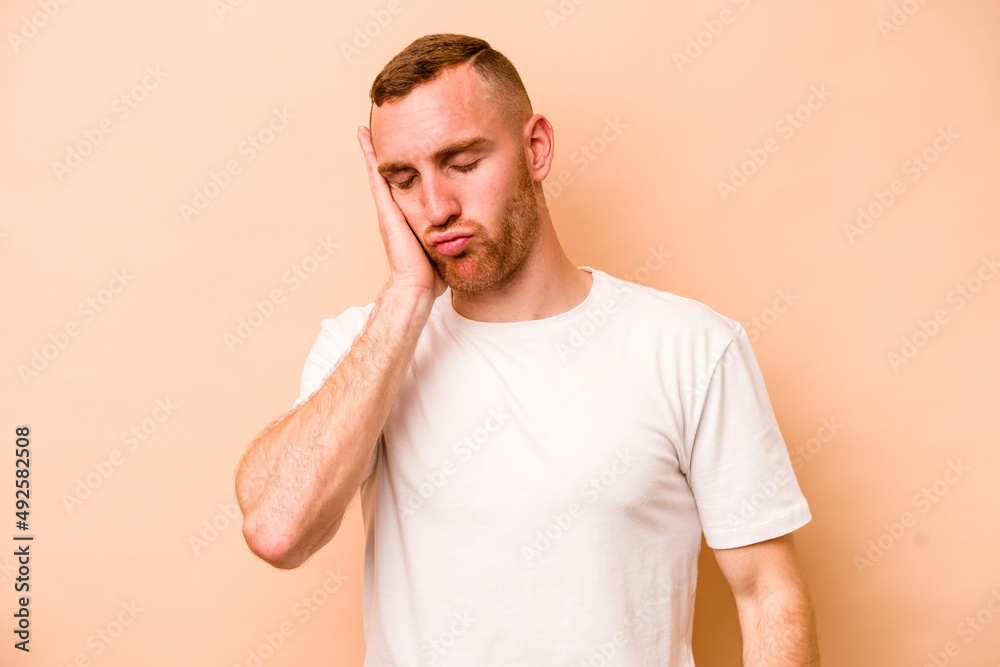 Young caucasian man isolated on beige background who is bored, fatigued and need a relax day.
