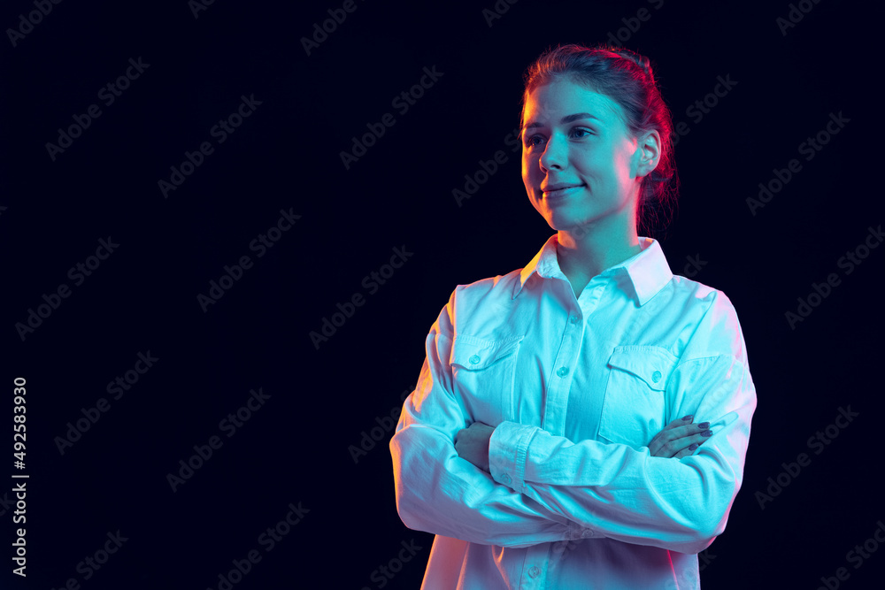 Half-length portrait of young pretty girl in white shirt isolated on dark background in blue neon light, filter. Concept of emotions, fashion, youth Half-length portrait of young pretty girl in white shirt isolated on dark background in blue neon light, filter. Concept of emotions, fashion, youth
