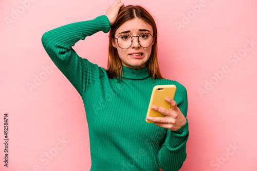 Young caucasian woman holding mobile phone isolated on pink background being shocked, she has remembered important meeting.