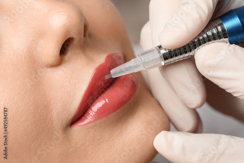 Young woman undergoing procedure of permanent lip makeup in salon, closeup