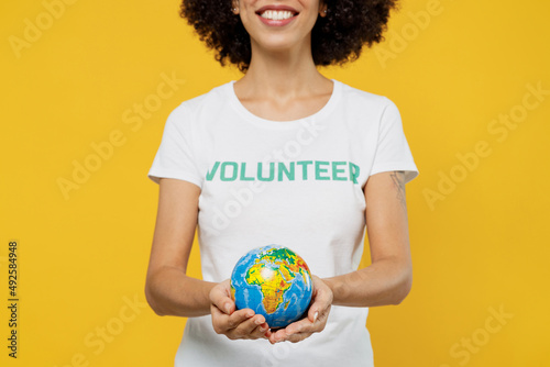 Cropped happy woman of African American ethnicity wears white volunteer t-shirt hold in palms Earth world globe isolated on plain yellow background. Voluntary free work assistance help grace concept. © ViDi Studio