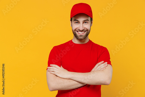 Professional delivery guy employee man in red cap T-shirt uniform workwear work as dealer courier hold hands crossed folded smile isolated on plain yellow background studio portrait. Service concept. © ViDi Studio