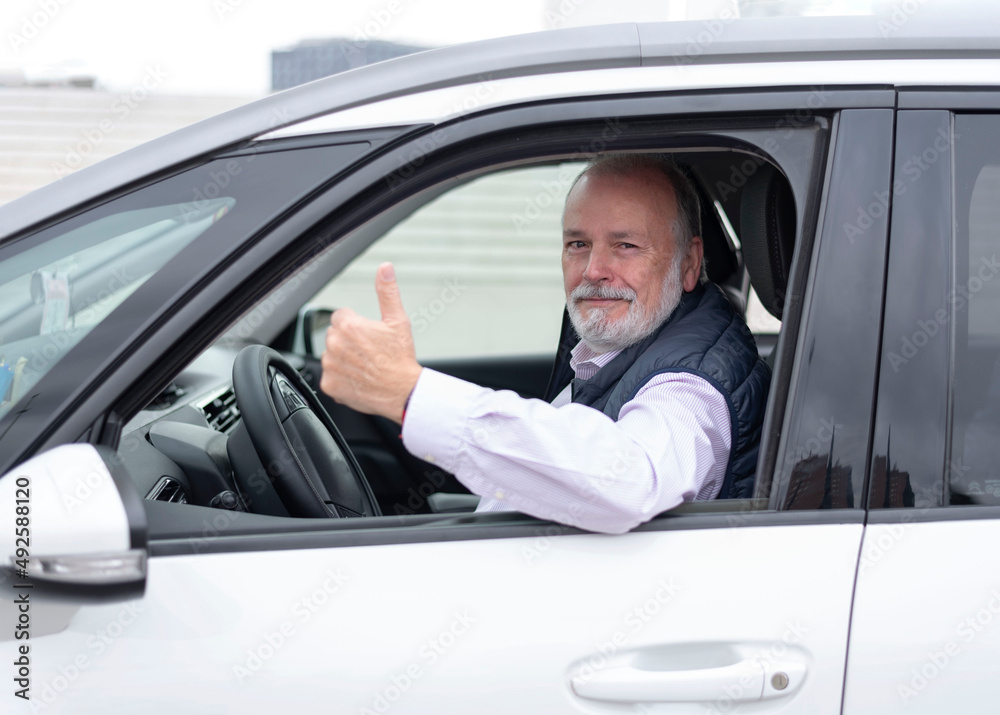 portrait of an elderly driver in car or taxi showing his thumb
