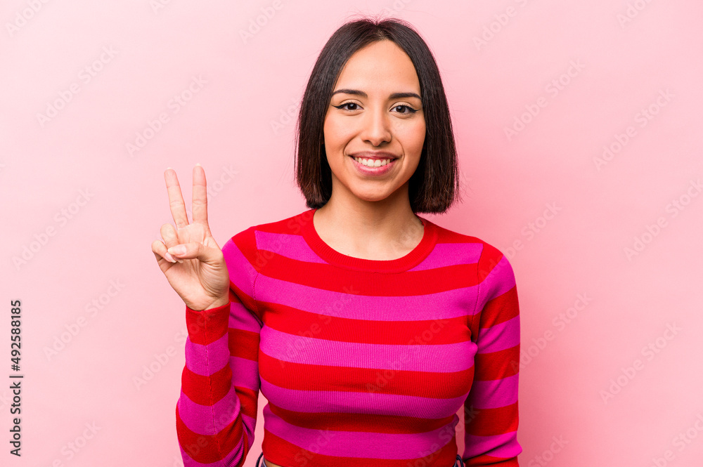 Young hispanic woman isolated on pink background showing victory sign and smiling broadly. Young hispanic woman isolated on pink background showing victory sign and smiling broadly.