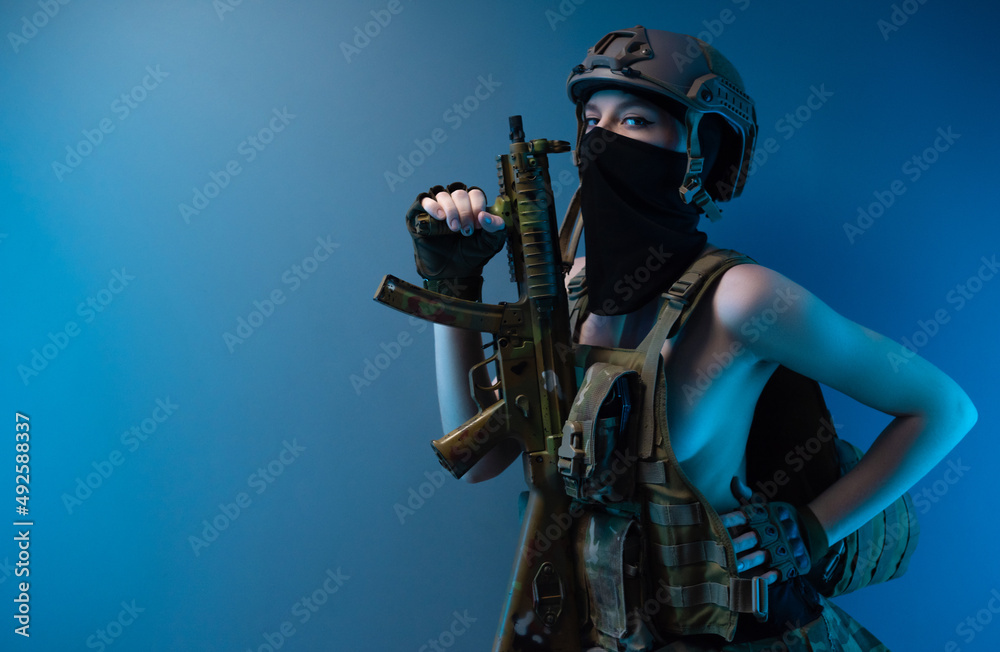 a naked girl soldier in a bulletproof vest and helmet, armed with an automatic rifle, in military clothes on a blue background