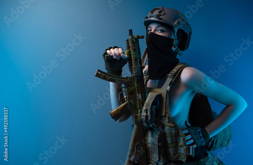 a naked girl soldier in a bulletproof vest and helmet, armed with an automatic rifle, in military clothes on a blue background