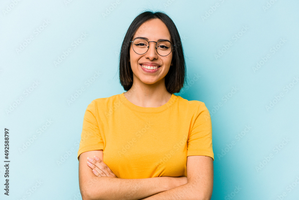 Fototapeta premium Young hispanic woman isolated on blue background who feels confident, crossing arms with determination.
