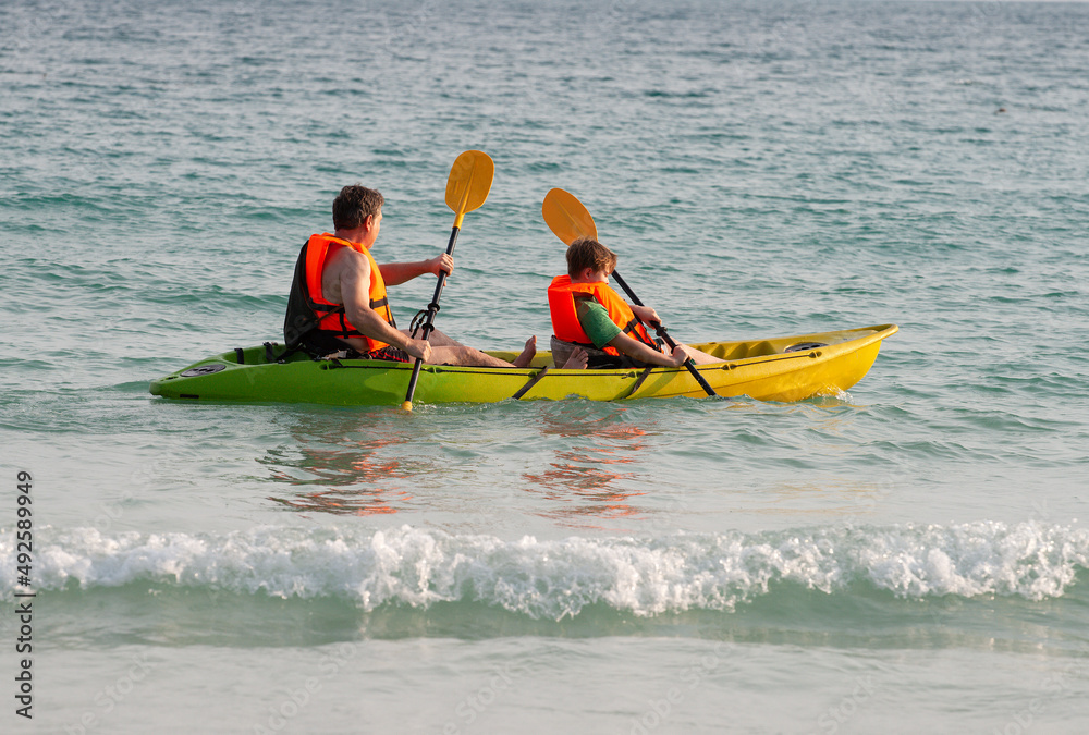 father and son enjoy paddling with the canoe at the sea