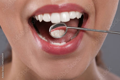 Examining woman's teeth with dentist's mirror on grey background, closeup