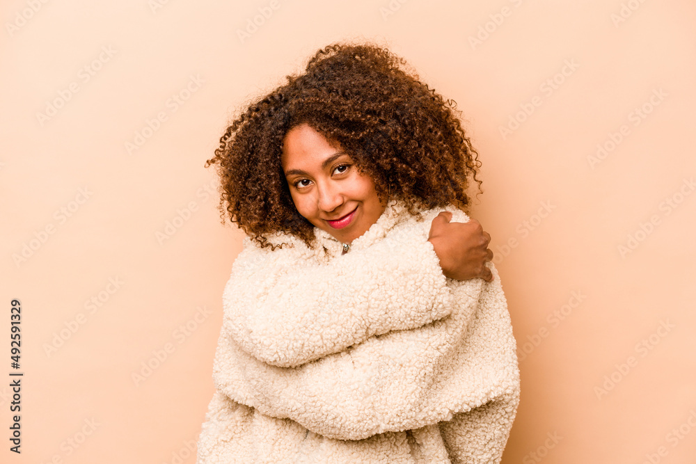 Young African American woman isolated on beige background hugs, smiling carefree and happy.