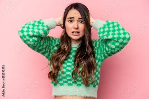 Young caucasian woman isolated on pink background covering ears with hands trying not to hear too loud sound. © Asier