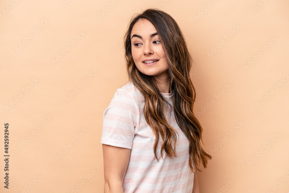 Young caucasian woman isolated on beige background looks aside smiling, cheerful and pleasant. Young caucasian woman isolated on beige background looks aside smiling, cheerful and pleasant.