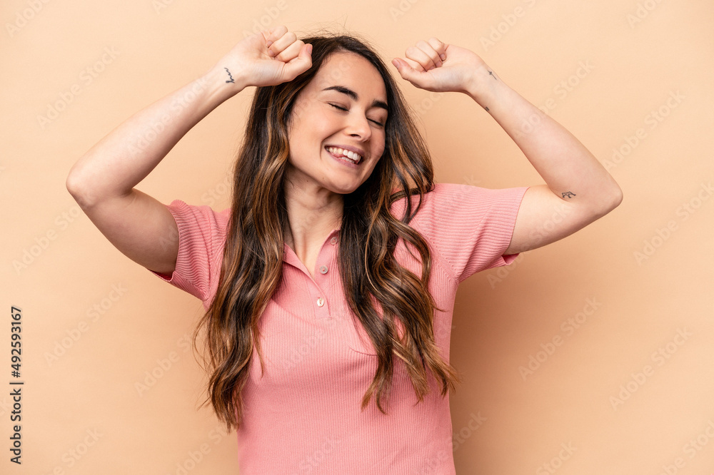 Young caucasian woman isolated on beige background celebrating a special day, jumps and raise arms with energy. Young caucasian woman isolated on beige background celebrating a special day, jumps and raise arms with energy.