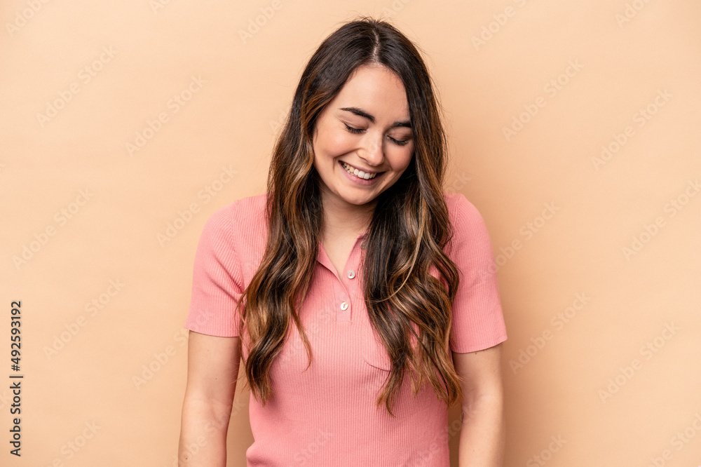 Young caucasian woman isolated on beige background laughs and closes eyes, feels relaxed and happy. Young caucasian woman isolated on beige background laughs and closes eyes, feels relaxed and happy.