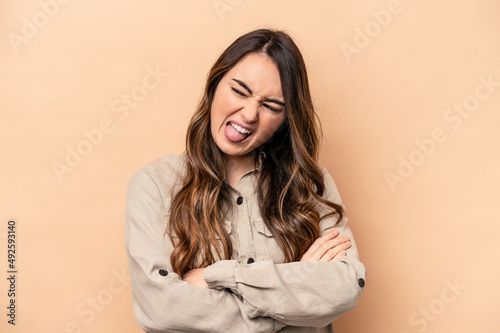 Young caucasian woman isolated on beige background funny and friendly sticking out tongue.