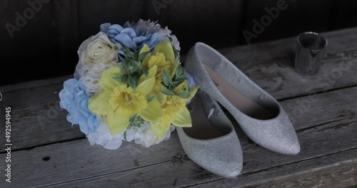 Brides blue, white and yellow bouquet with her silver heels laid out as a flat lay on a wooden bench. photo