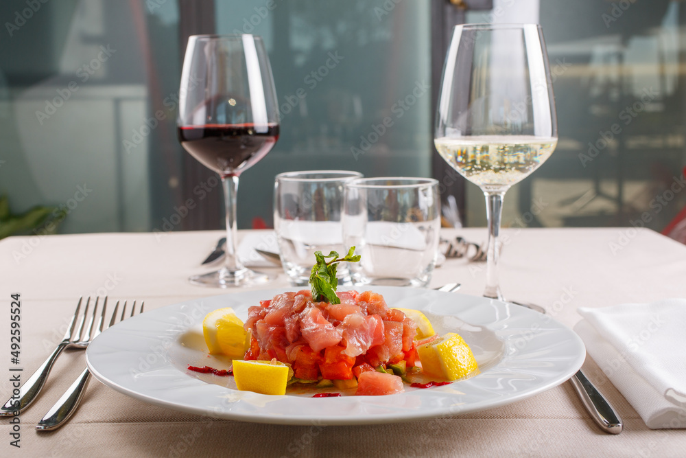 Tartare di ricciola e tonno rosso servita come antipasto in un ristorante elegante con due calici di vino rosso e bianco