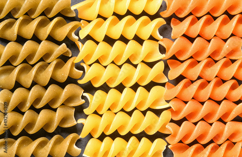 Tri-color fusilli dry pasta in Italian flag pattern top view background on dark background