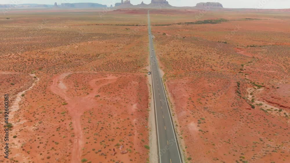 Drone follows silver car driving along famous sunny American desert highway road in Monuments Valley in Arizona and Utah