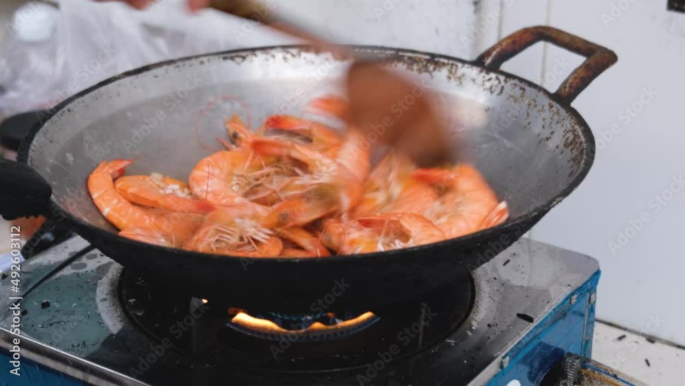The chef is cooking shrimp with salt in an iron pan. The chef is cooking shrimp with salt in an iron pan.