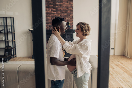 Young african man embraces his caucasian pregnant woman and touches her belly.