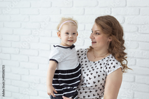 Mother holds her child with hearing aids and cochlear implants on white brick wall with copy space and place for advertising . Deaf and health concept