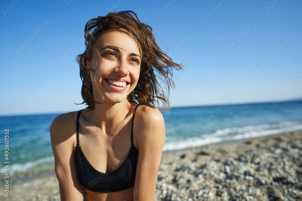 Fototapeta premium Outdoor shot of smiling young female model enjoying at sea beach against blue sky. Woman having fun out on a summer day.