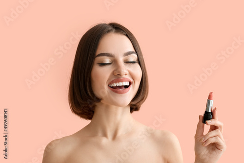 Happy woman with closed eyes holding lipstick on color background