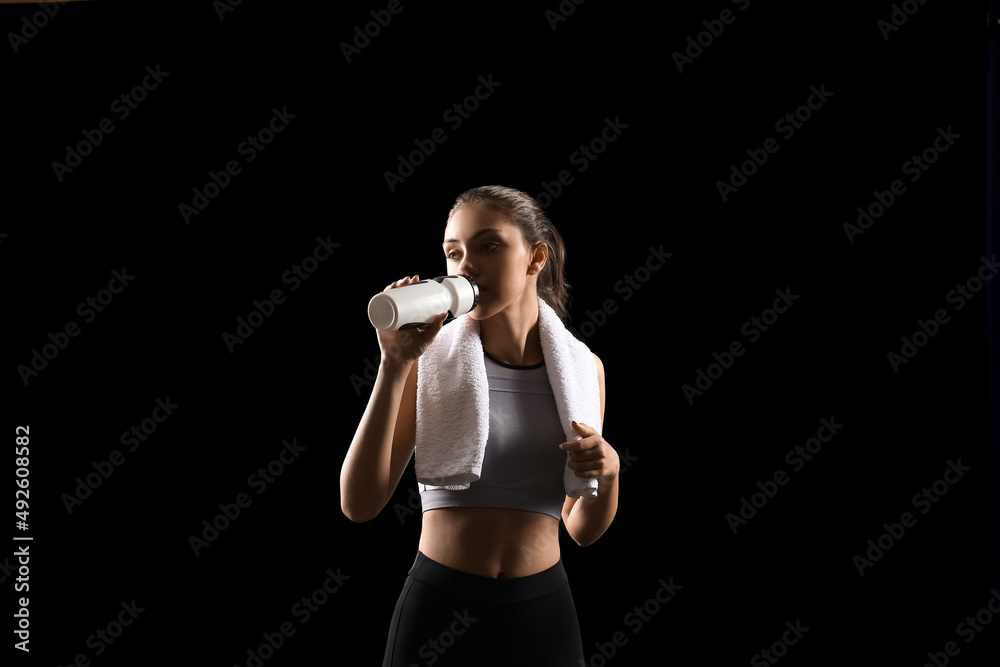 Sporty teenage girl with towel drinking water on black background Sporty teenage girl with towel drinking water on black background
