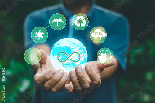 A man's hand holds the globe that envelops a bright atmosphere. with icons related to the circular economy Increased energy consumption and CO2 emissions, energy savings. natural energy use