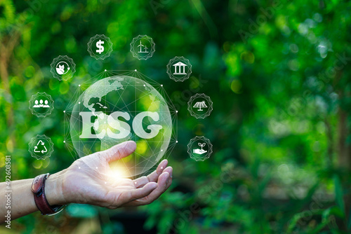 Man's hand holding a globe with ESG icon for the environment, society, and governance in sustainable and ethical business. and network connection on a green background.