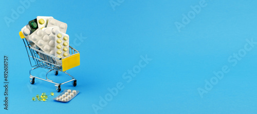 Blisters with pills of different types in a shopping trolley on a blue background, copy space, banner