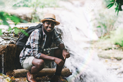 African Man Traveller holding a film camera with backpack sitting and relaxing freedom at the waterfall.