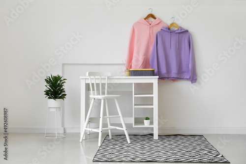 Table with organizer and stylish hoodies hanging on light wall © Pixel-Shot