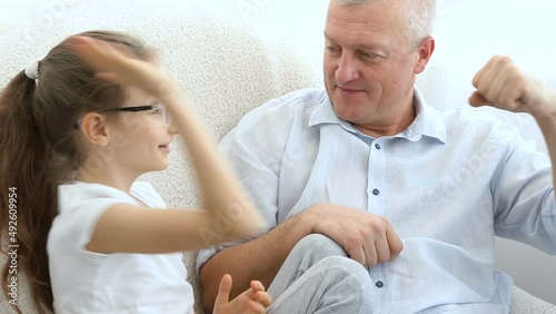 Indoor portrait of grey-haired father and little blonde girl playing with each other at home, father's day concept.
