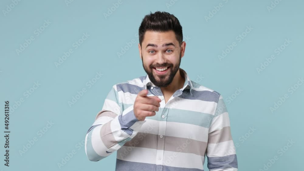 Cheerful happy young bearded brunet man 20s wear striped shirt look around for friend find waving meet greet with hand as notices someone isolated on plain pastel light blue background studio portrait Cheerful happy young bearded brunet man 20s wear striped shirt look around for friend find waving meet greet with hand as notices someone isolated on plain pastel light blue background studio portrait